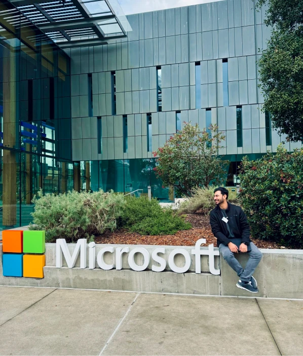 A man sitting on a large Microsoft sign outside a glass office building
