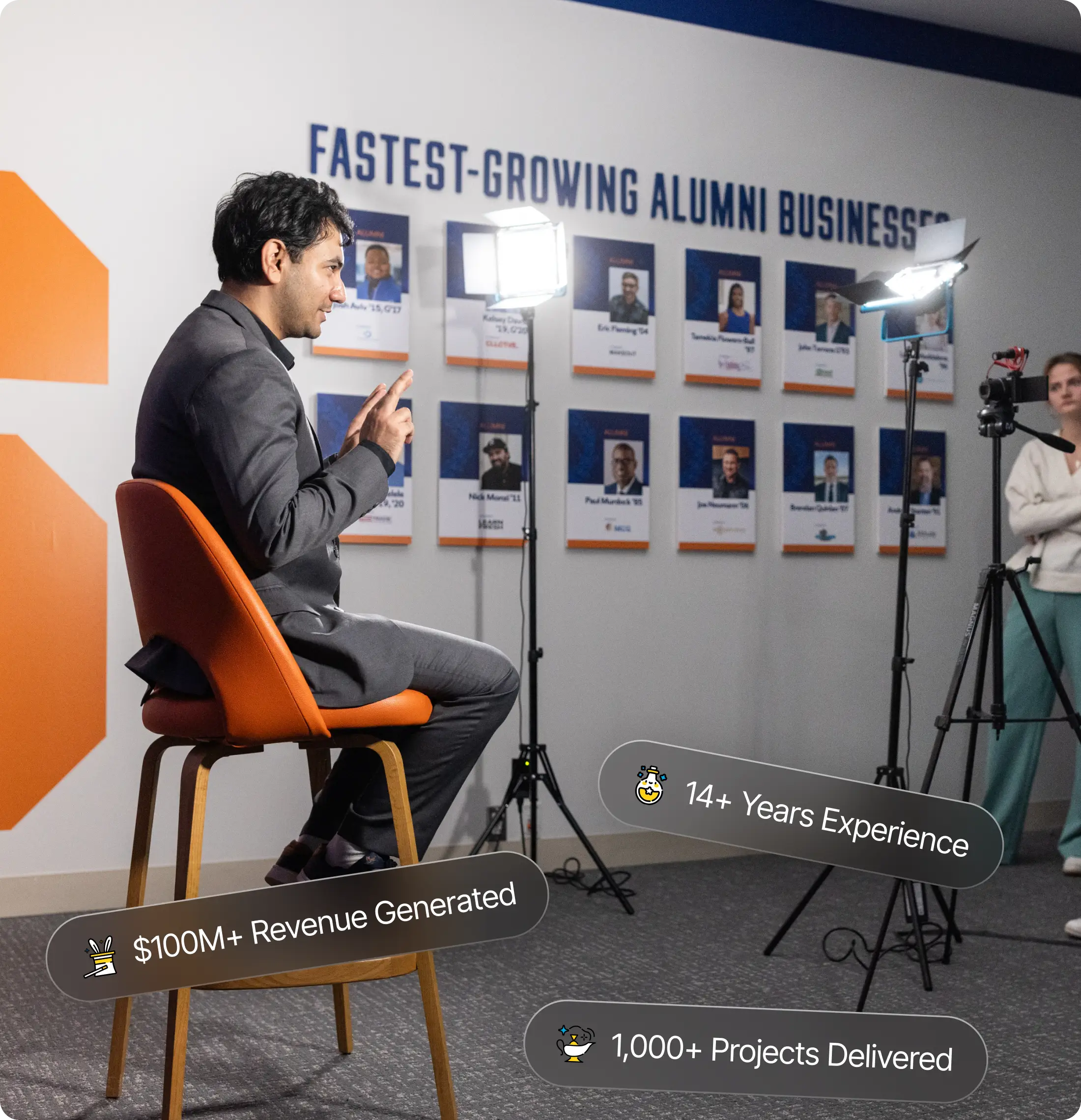 meeting A man in a gray suit sitting on an orange chair in front of a wall with a sign that says 'Fastest-Growing Alumni