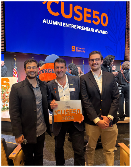 Three men at the 'Cuse50 Alumni Entrepreneur Award, one holding a 'Cuse50 2024 sign, Syracuse University on screen