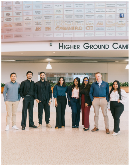 A group of nine people standing in a row in a bright university hall
