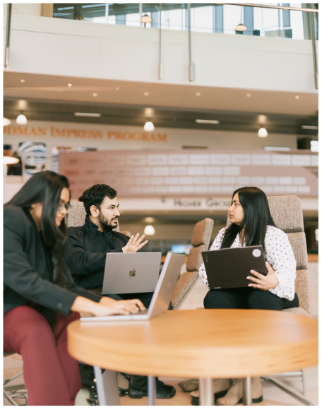 Three people talking around a table with laptops in a university hall