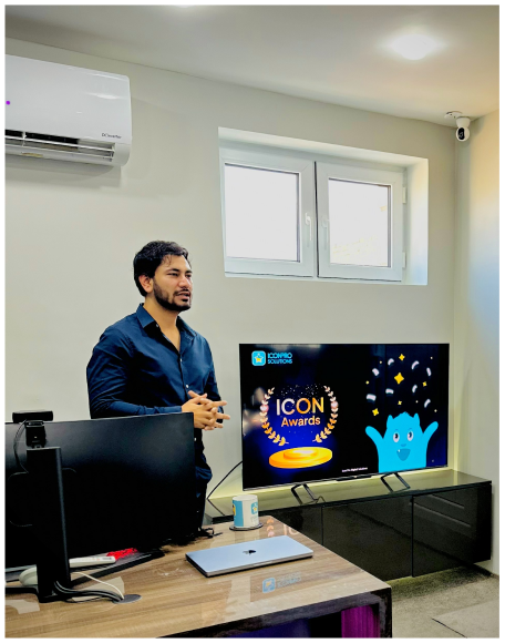 A man seated at a desk beside a TV that shows an ICON Awards graphic