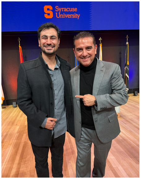 Two men posing together in front of a Syracuse University screen at an event