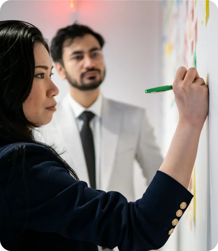 A woman sketching ideas on a whiteboard while a colleague watches