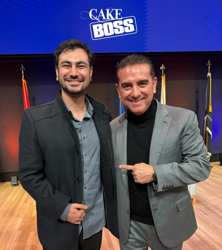 Waqar Hussain, Icon Pro Solutions CEO, smiling with another man at a Syracuse University event in front of a Cake Boss slide