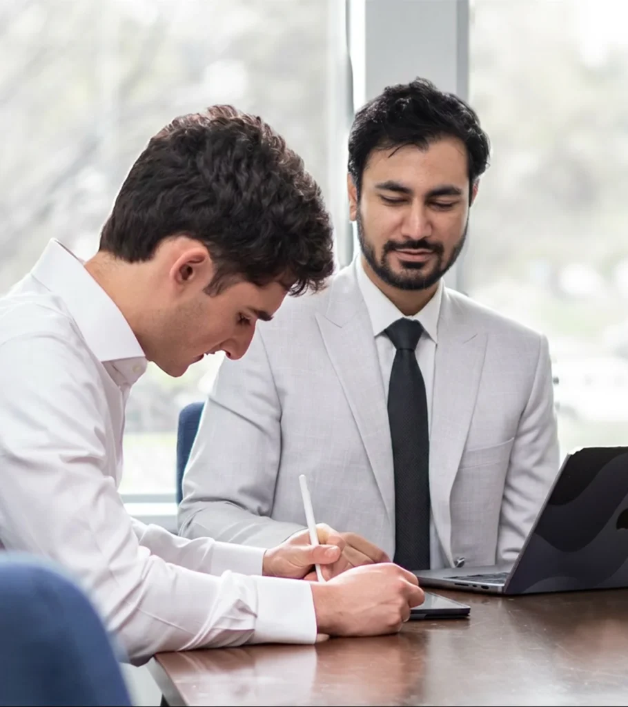 Waqar Hussain, Icon Pro Solutions CEO, in a suit reviewing work on a laptop with another man