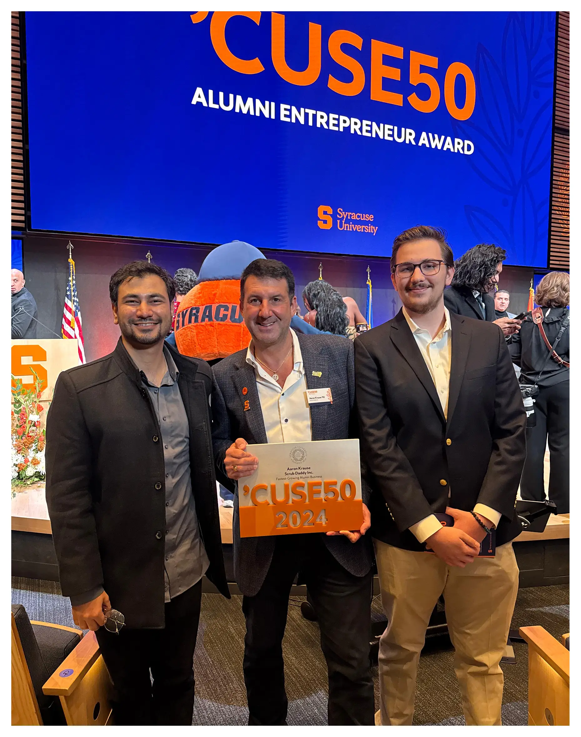 Three men at the Syracuse University 'Cuse50 Alumni Entrepreneur Award, one holding a 'Cuse50 2024 sign