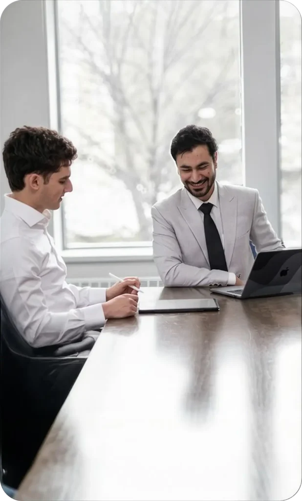 Two men talking across a meeting table with a laptop